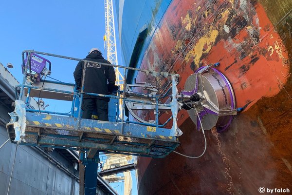 technician operating an automated heli-washing machine on a vessel’s outer hull during shipyard maintenance.